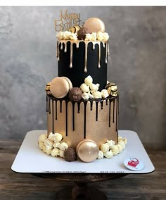 a black and gold birthday cake with chocolate drizzled on it's sides