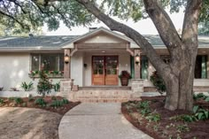 a white house with a tree in front of it and landscaping around the porch area