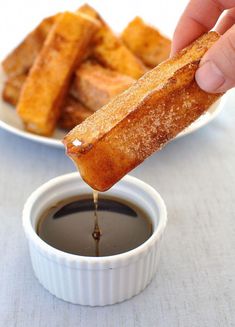 someone is dipping something into a small bowl of sauce on a plate with bread sticks