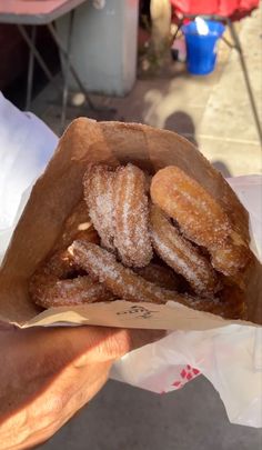 a person holding a brown paper bag filled with sugar covered doughnuts on top of it