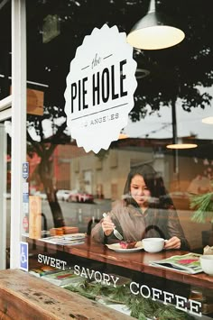 a woman sitting at a table in front of a store window with food on it