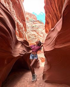 a woman standing in the middle of a narrow slot between two large red rocks, with her hands on her head