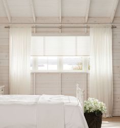 a white bed sitting under a window next to a wooden table with flowers on it