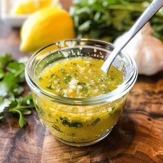 a glass jar filled with yellow liquid sitting on top of a wooden cutting board next to lemons and parsley