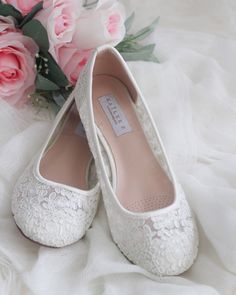 a pair of white wedding shoes sitting on top of a bed next to pink flowers