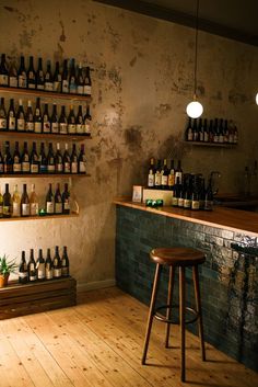 there is a bar with many bottles on the wall and stools in front of it