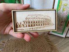 a hand holding up a small wooden frame with an image of a building on it