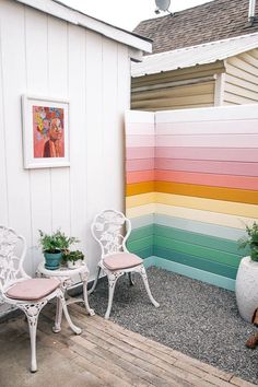 two white chairs sitting next to each other in front of a rainbow colored wall and potted plants