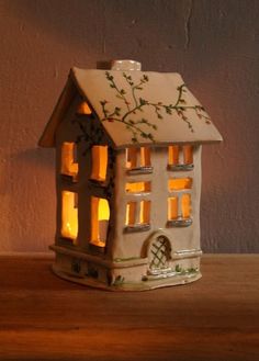 a lit up house shaped candle holder sitting on a wooden table next to a wall