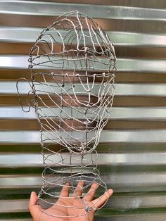 a hand reaching out from behind a wire sculpture that looks like a human's head