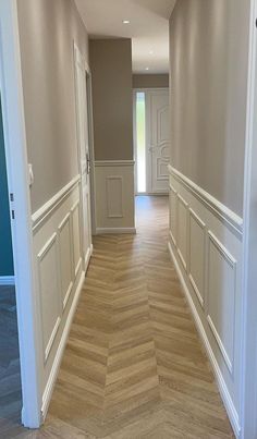 an empty hallway with wood flooring and white trim on the walls, leading to another room