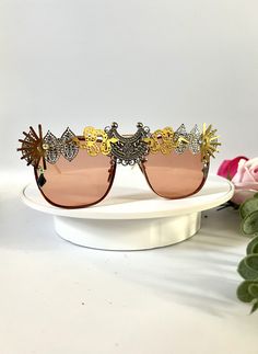 💛Unisex rose gold statement sunglasses by Alexis Exclusive. 💛These unique glasses will add that special touch to your summer / festival / holiday outfits... Be the one and only person in this unique design. 💛The frames are oversized and they have tinted rose gold/orange lenses. All along the top they have been designed in a mixture of funky jewels, embellishments and trinkets. 💛A medium weight design that are comfortable to wear. 💛Great for festivals, weddings, holidays, burning man or everyday wear to add some glam to your outfits.  💛Light UV protection. 💛Exclusive design made by myself, you won't see any others like these anywhere else. 💛All my glasses come in a black branded pouch to keep them safe, please also handle with care. 💛Checkout the full collection of Sunnies here : Elegant Gold Shield Sunglasses For Summer, Gold Mirrored Shield Sunglasses For Parties, Party Sunglasses With Metal Frame And Glass, Summer Party Sunglasses With Mirrored Lenses, Gold Metal Frame Sunglasses For Party, Gold Summer Sunglasses With Uv Protection, Elegant Shield Sunglasses For Summer Party, Trendy Metal Sunglasses For Festivals, Elegant Gold Sunglasses For Summer