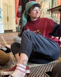 a young man sitting on the floor with his foot up in front of him, smiling