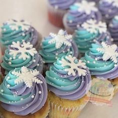 cupcakes with blue frosting and white snowflakes on them are displayed