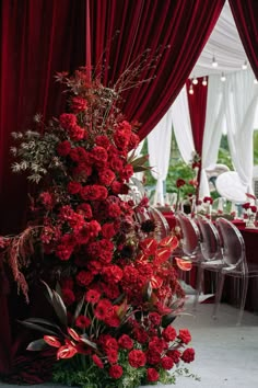 red flowers and greenery are arranged on the floor in front of curtains at an event