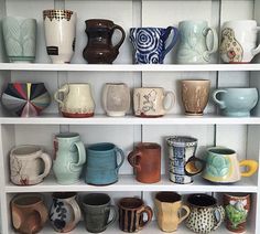 a shelf filled with lots of different colored coffee mugs on top of white shelves