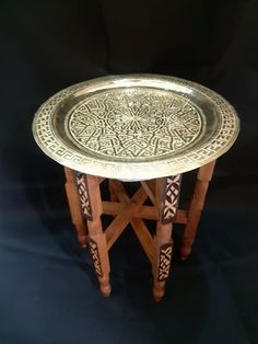 an ornately decorated table with wooden legs and a metal tray on it's side