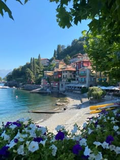 the beach is lined with flowers and houses on the hill above it, along with boats in the water