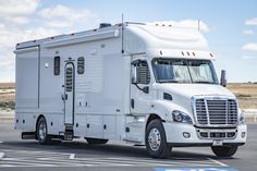 a large white truck parked in a parking lot next to a field and blue sky