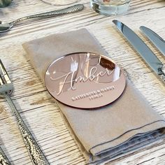 a place setting with silverware and napkins on a wooden table top, along with a personalized name plate