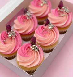 cupcakes with pink frosting and silver decorations in a box on a table