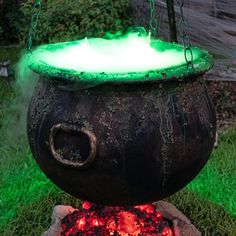 an old caulder with glowing green lights in the grass next to a fire pit