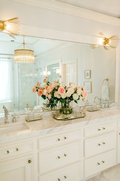 a bathroom vanity with flowers in a vase on the counter and two mirrors above it