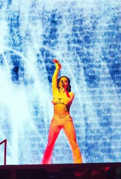 a woman in yellow is performing on stage with her arms up and hands behind her head