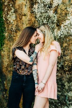 two women standing next to each other in front of a wall with moss growing on it