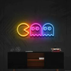 a neon sign with two ghost faces on it in front of a black wall and sideboard