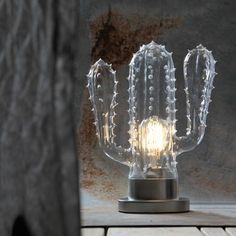 a glass cactus lamp sitting on top of a metal stand next to a tree trunk