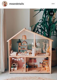 a wooden doll house with lots of furniture and accessories on display in front of a potted plant