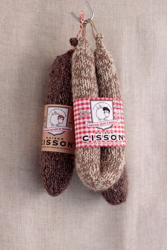 two brown and white knitted mittens hanging from a hook on a beige cloth