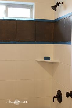 a white bathroom with black and blue trim on the shower head, shelf above the toilet