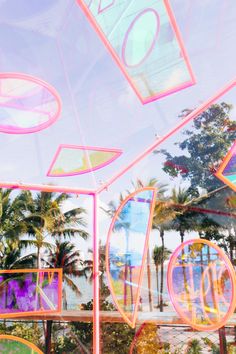 the reflection of palm trees and buildings in a glass window with pink, blue, yellow and green shapes