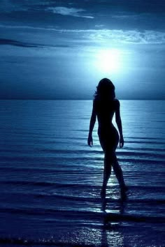 a woman standing in the ocean at night with her back turned to the camera,