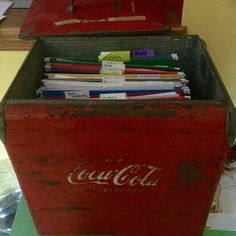 an old coca - cola cooler is filled with files and folders on a table