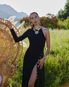 a woman in a black dress standing next to a wicker basket and wearing earrings