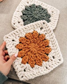 someone is crocheting an orange and green flower on a blanket