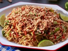 a white plate topped with noodles and veggies next to sliced lime wedges