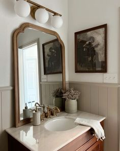 a bathroom sink with a mirror above it and two pictures on the wall behind it