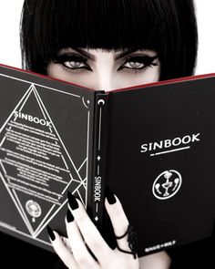 a woman with black hair holding up a book in front of her face and looking at the camera