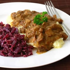 a white plate topped with meat and gravy covered in gravy next to red cabbage