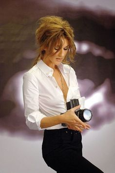 a woman is holding a camera in her right hand and looking down at the ground