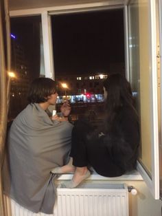 two people sitting on a window sill looking out at the city