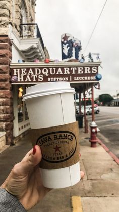 a person holding up a cup of coffee in front of a building with a sign on it