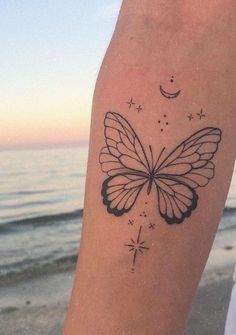 a person with a butterfly tattoo on their arm and the ocean in the back ground