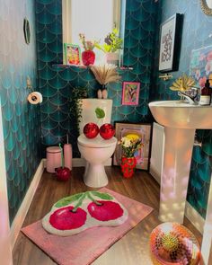 a bathroom decorated in pink, green and blue with apples on the rug next to the toilet