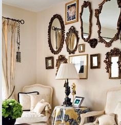 a living room filled with white furniture and lots of mirrors on the wall above it