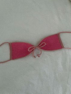 a pink crocheted bow tie laying on top of a white sheet with red thread